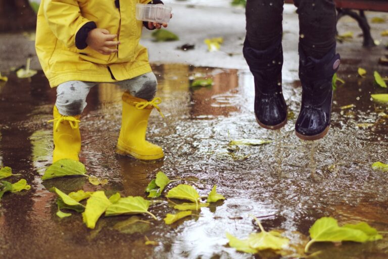 Tout-petit équipé de bottes de pluie et d'un ciré jaune dans une flaque d'automne