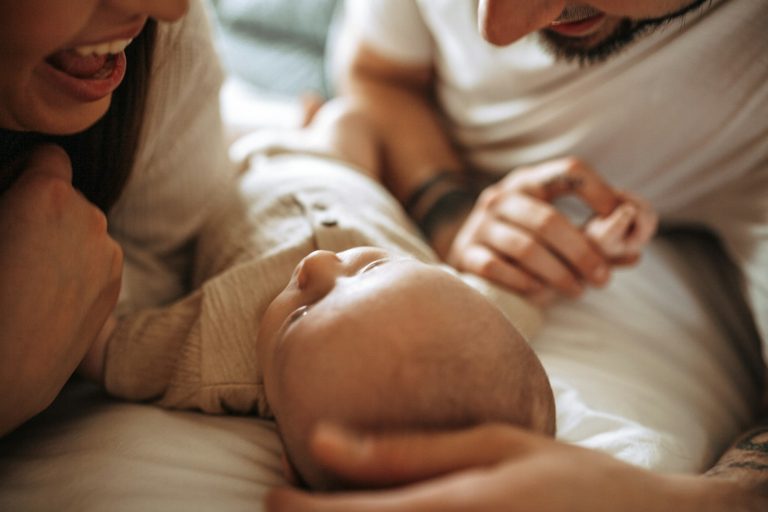 Parents souriants penchés sur leur nouveau-né allongé sur le lit, de retour à la maison